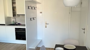 A modern kitchen with white cabinets, a built-in oven, and a dining area with a dark table and white chairs. - Terrace Flair (Wien)