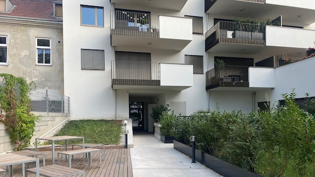 A modern apartment building with multiple balconies, a wooden deck, and a small garden area. - Terrace Flair (Wien)