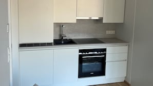A compact kitchen with white cabinetry, a built-in oven, and a sink. - Terrace Flair (Wien)