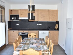 Una cocina moderna con armarios de madera, encimera negra, microondas Bosch, refrigerador Liebherr y una mesa de comedor con azulejos.