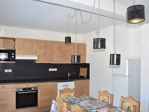 Ett modernt kök med träskåp, en svart bänkskiva, en Bosch-mikrovågsugn, en spis och ett matbord med stolar.