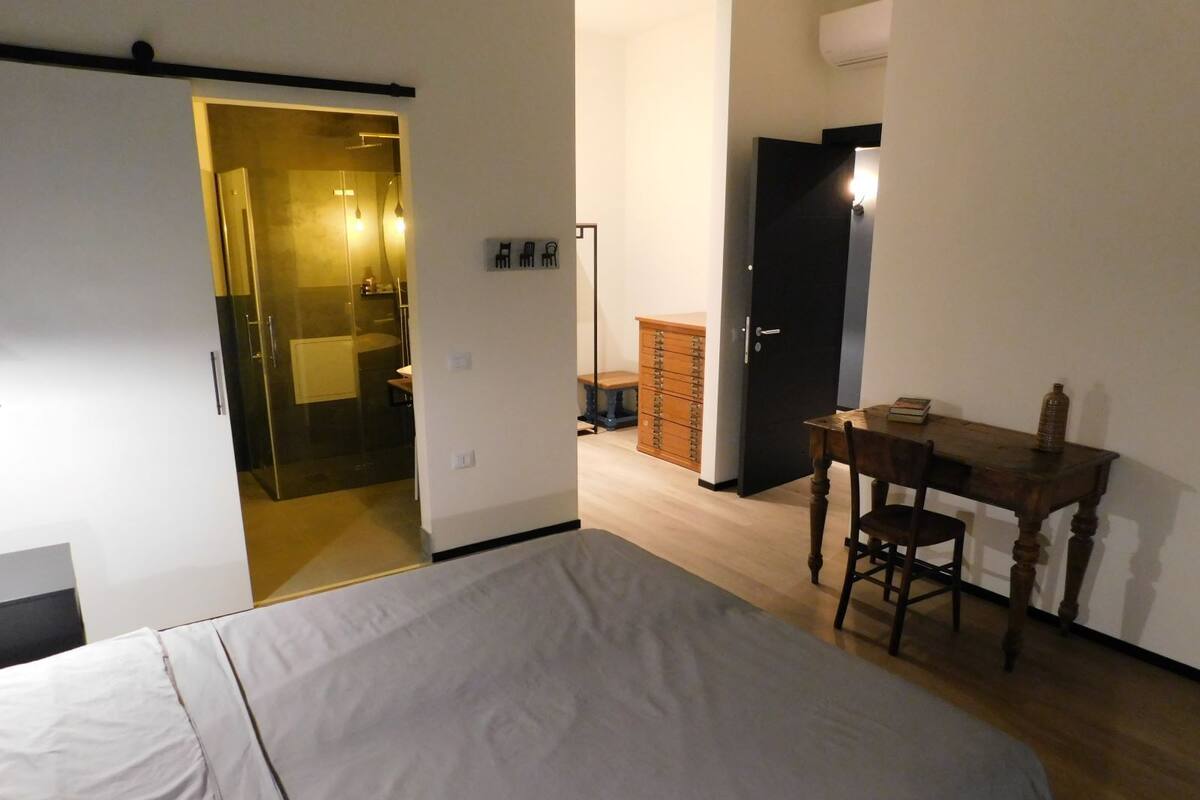A bedroom with a bed, a wooden desk, a chair, a wardrobe, and a bathroom visible through an open door.