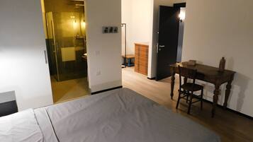Une chambre à coucher avec un lit, un bureau en bois, une chaise, une armoire et une salle de bain visible à travers une porte ouverte.