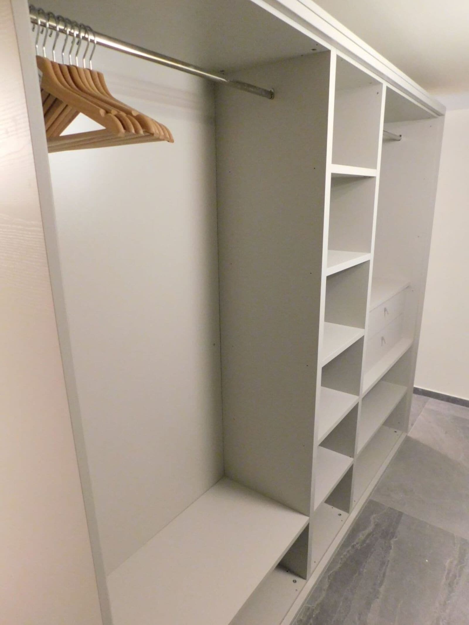 Ein begehbarer Kleiderschrank mit offenen Regalen und einer Kleiderstange aus Holz.