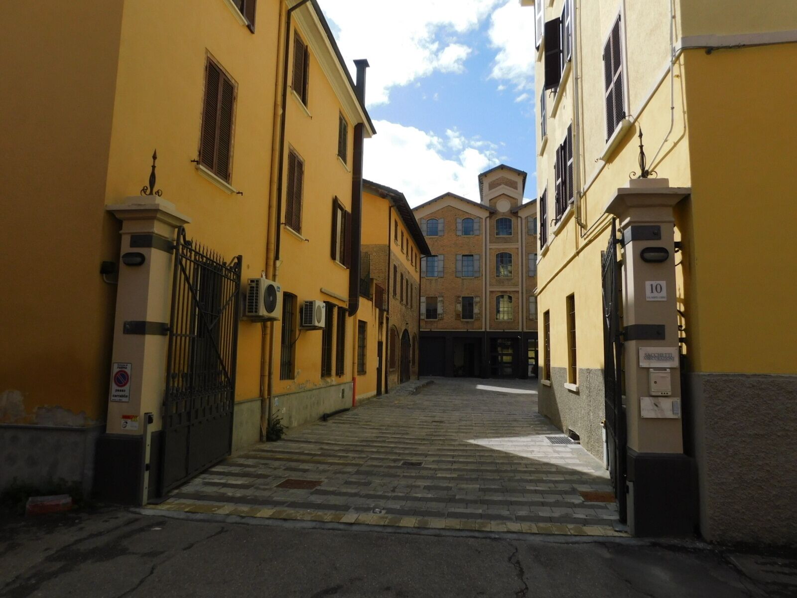 A narrow street with yellow buildings, a gated entrance, and a clear sky.