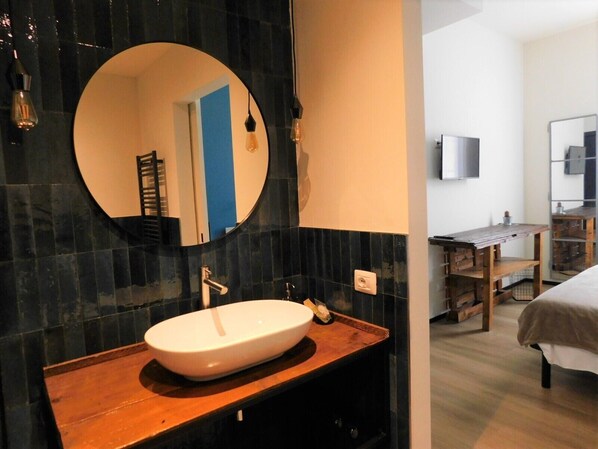 A modern bathroom with a round mirror, a white sink, and a wooden vanity. - Piumaviola (Parma)