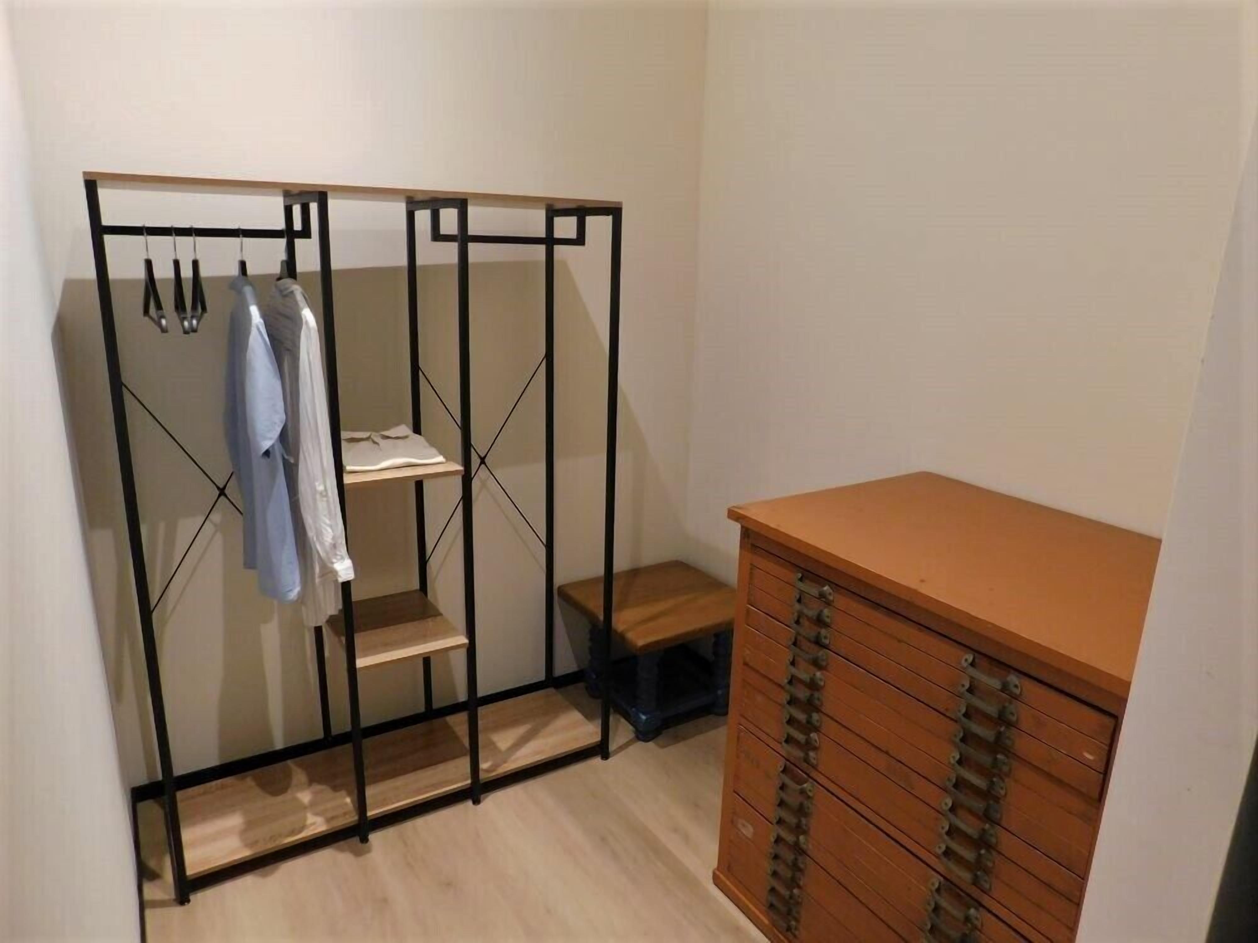 A walk-in closet with a metal frame, shelves, and a wooden dresser.