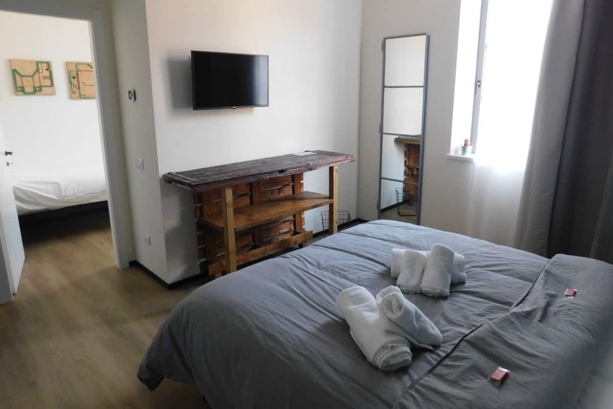 A bedroom with a bed, a wooden bench, a flat-screen TV, and a mirror.
