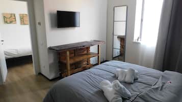 Un dormitorio con cama, un banco de madera, un televisor de pantalla plana y un espejo.
