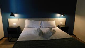 Habitación de hotel con una cama bien hecha, dos lámparas de noche y un enchufe en la mesita de noche.