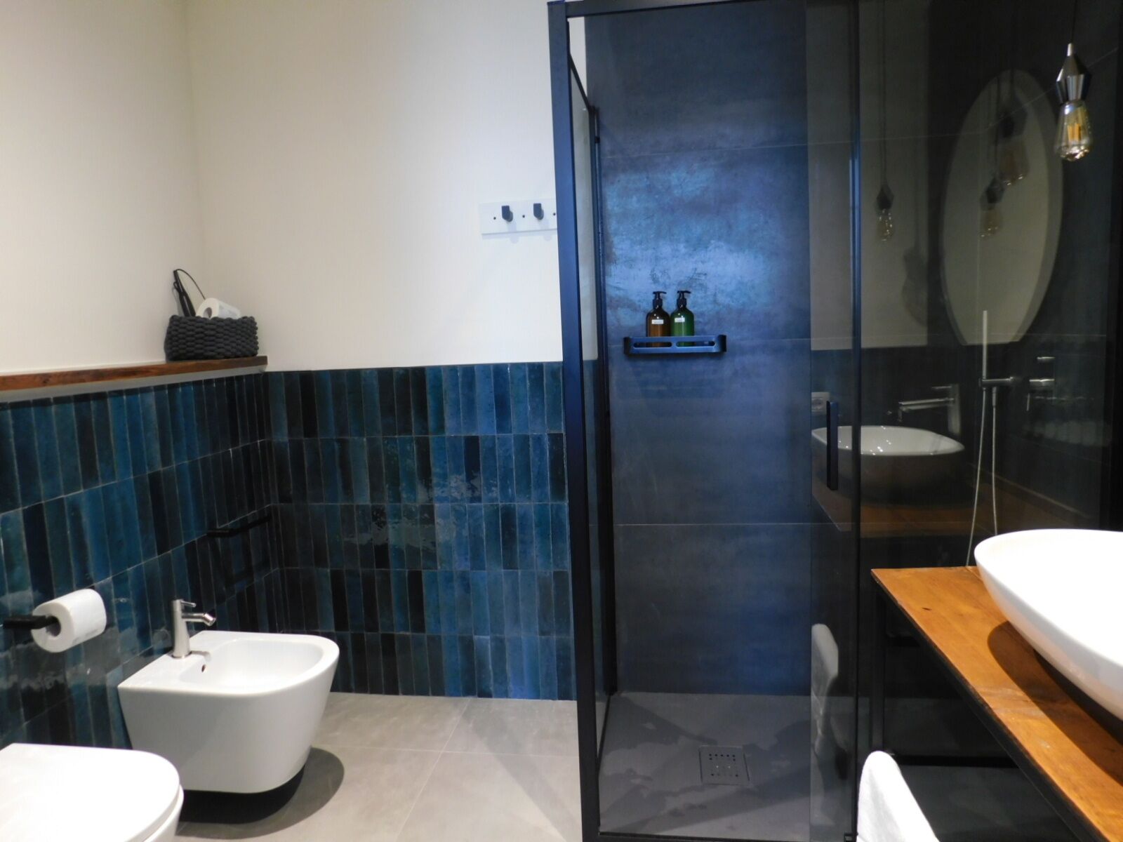 Een moderne badkamer met een bidet, een douchecabine met glazen wanden en een houten wastafelmeubel.