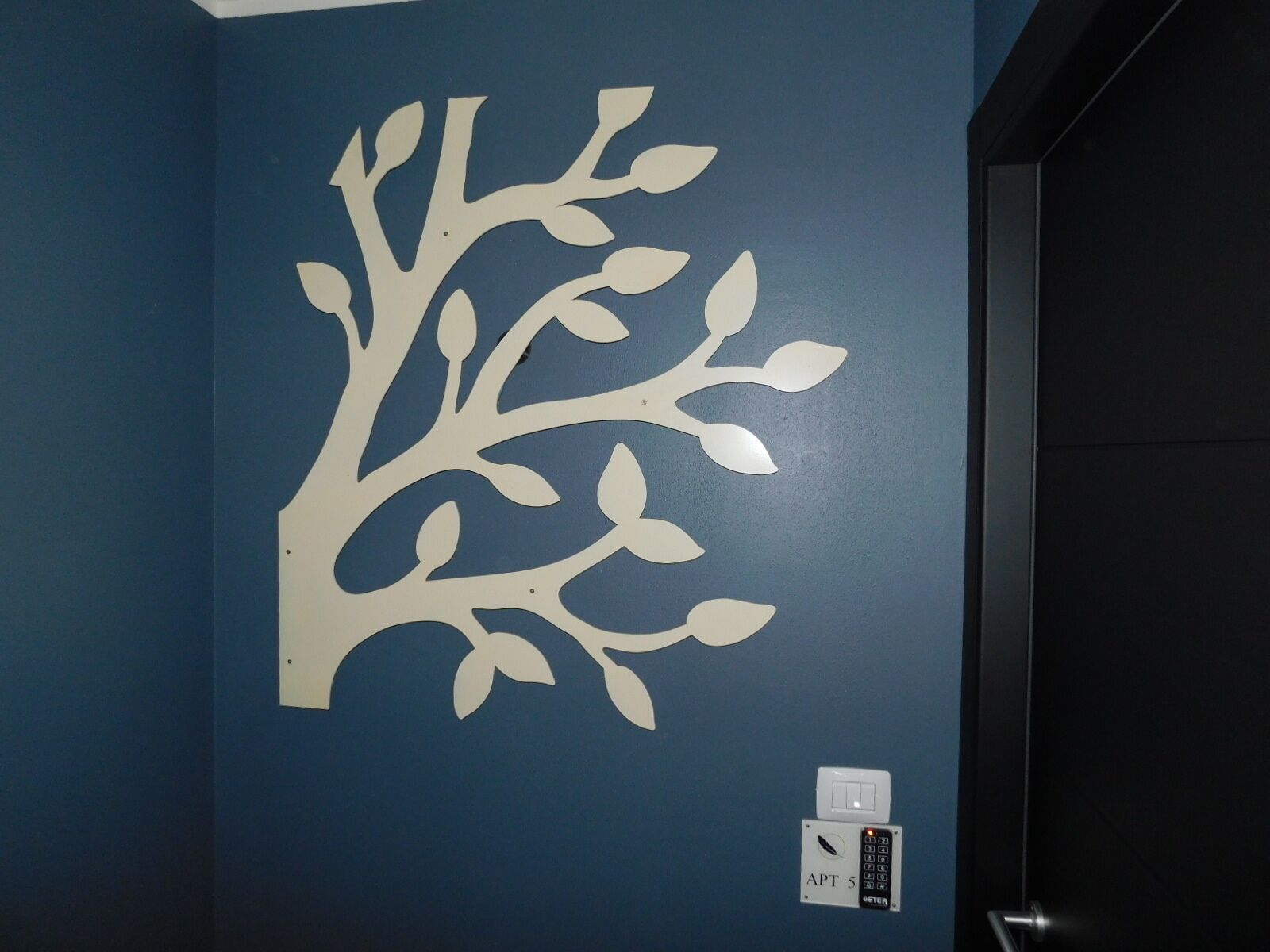 A wall with a white tree decal and a door with a control panel.