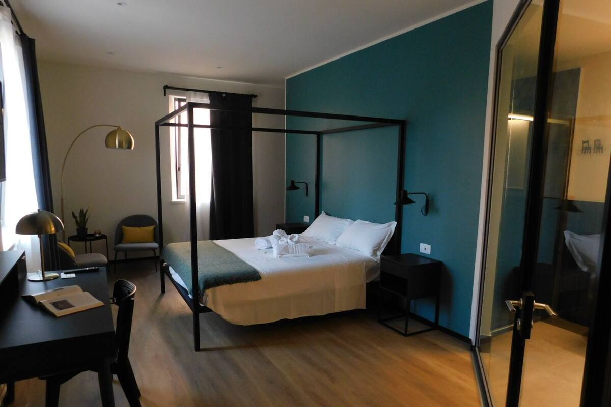 A modern bedroom with a four-poster bed, a desk with a lamp, and a chair.
