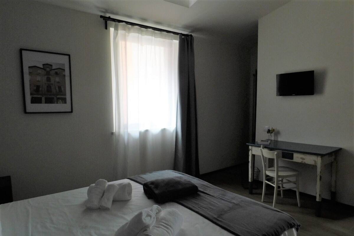 A hotel room with a bed, a desk, a chair, a TV, and a window with curtains.
