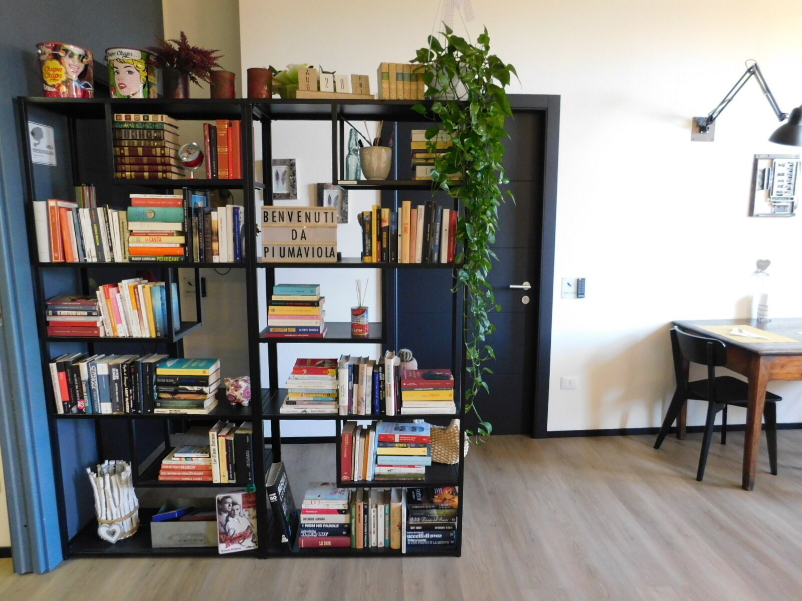 Ein Zimmer mit Bücherregal, Schreibtisch, Stuhl und einer Zimmerpflanze.