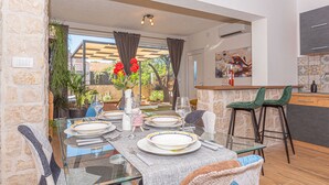 Comedor con una mesa de vidrio dispuesta para cuatro personas, rodeado de paredes de piedra y vistas al exterior.