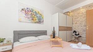 Un dormitorio moderno con una cama grande, una mesita de noche con una botella y vasos, una pared de piedra y un cuadro en la pared.