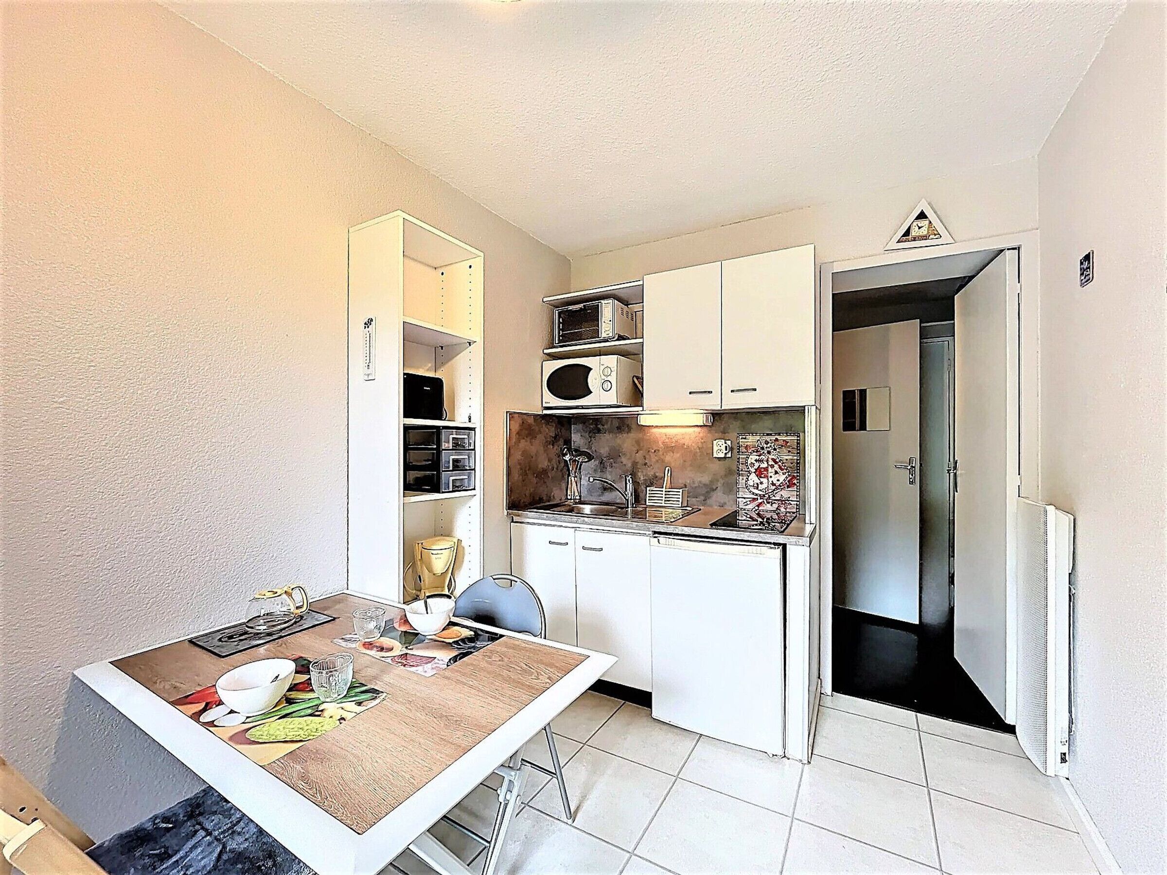 A compact kitchen with white cabinets, a microwave, and a sink. A dining table with a chair is positioned in front of the kitchen.
