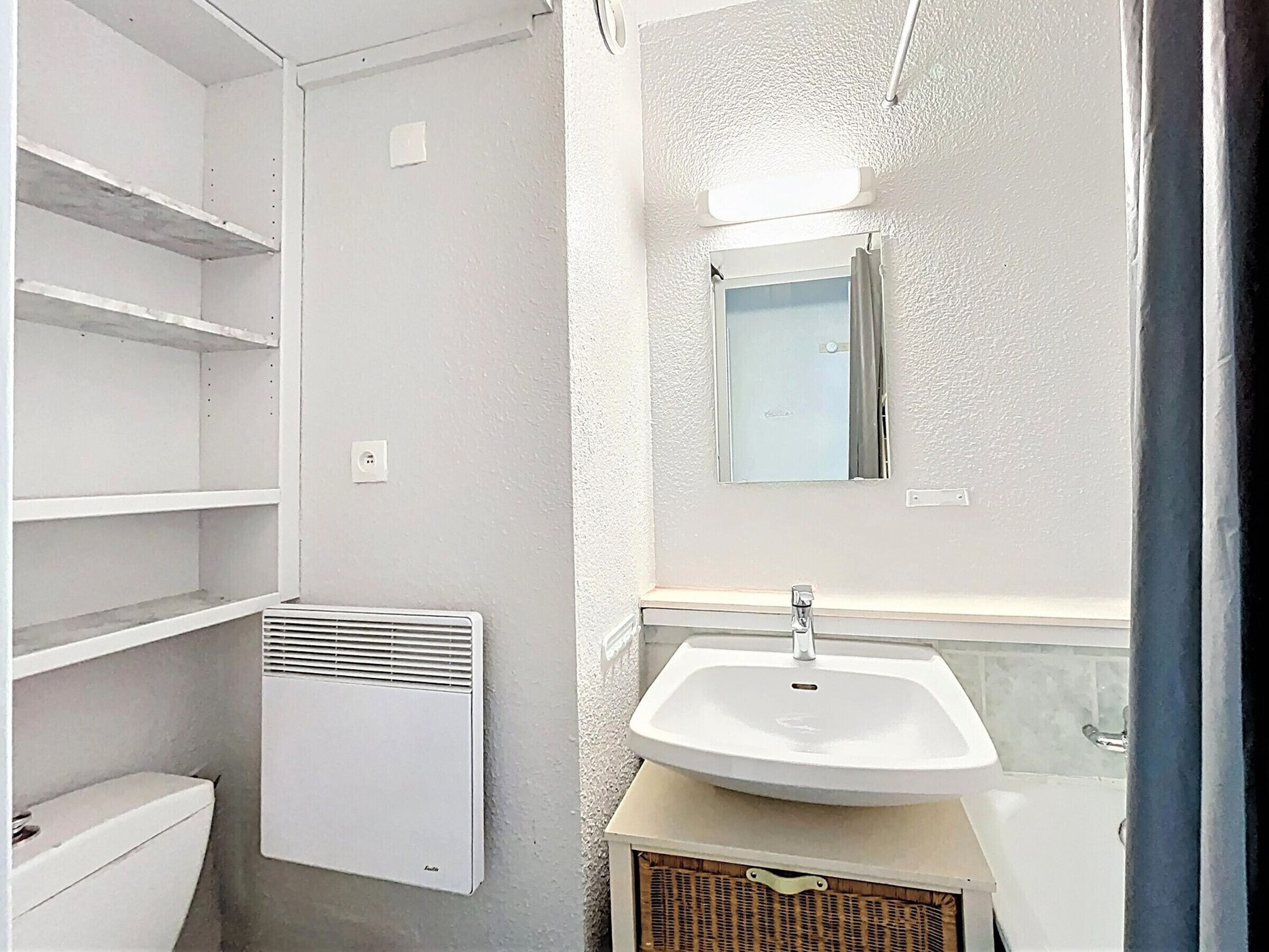 Ein Badezimmer mit einem weißen Waschbecken, einem Spiegel und einer Lüftungsanlage.