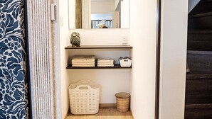A narrow hallway with a wooden floor, a mirror on the wall, and a shelf with folded towels and a basket. - Shirakawa Seiryuan (Kyoto)