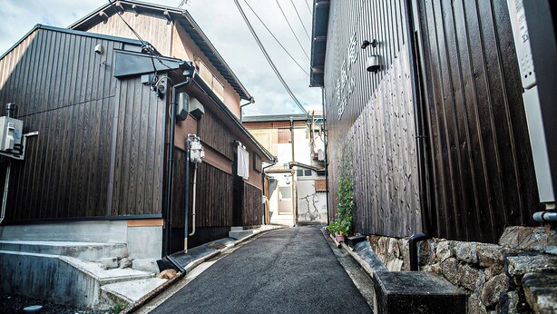A narrow alleyway between wooden buildings with visible pipes and a small step leading to a door. - Shirakawa Seiryuan (Kyoto)
