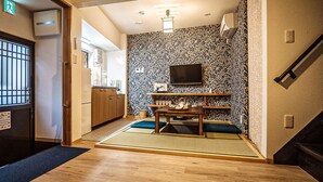 A traditional Japanese room with tatami flooring, a low table with tea set, a television on the wall, and a sliding door with a sign. - Shirakawa Seiryuan (Kyoto)