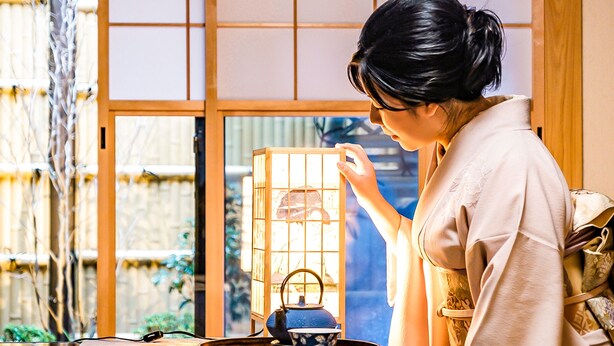 A person in traditional attire standing by a window with a lantern. - Chiyonoya (Kyoto)