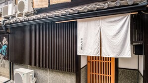 A traditional Japanese building with a black sliding door, a white cloth hanging, and air conditioning units. - Chiyonoya (Kyoto)
