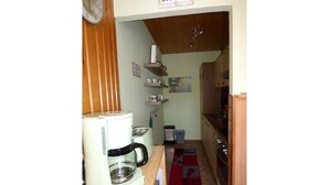 Una cucina compatta con macchina da caffè, tostapane e forno a microonde. Si nota un pensile in legno e un piccolo ripiano con tazze e una fotografia.