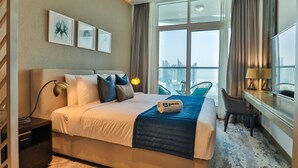 A hotel room with a large bed, a desk with a chair, a view of the city through large windows, and artwork on the wall. - HiGuests - DAMAC Maison Prive Tower A (Dubai)