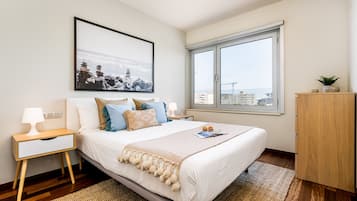 Une chambre à coucher bien rangée, avec un lit, une table de chevet, une lampe et une fenêtre donnant sur la ville.