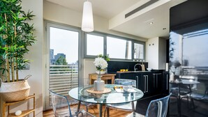 A modern kitchen with a glass dining table, clear chairs, and a potted plant.
