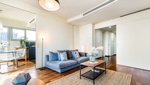 A modern living room with a sofa, coffee table, and a dining area with a glass table and chairs.