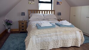Une chambre à coucher comprenant un lit, deux tables de chevet, une commode, une coiffeuse, une fenêtre et un mur orné de deux tableaux.