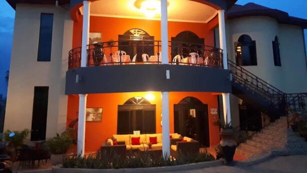 A two-story building with a balcony on the upper floor, a staircase leading to the entrance, and a well-lit entrance area. - Puma Garden and Suites (Kigali)