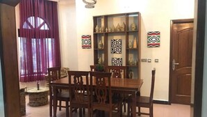 A dining area with a wooden table and chairs, a decorative shelf with vases, and patterned wall art. - Puma Garden and Suites (Kigali)