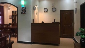 A reception area with a wooden desk, a clock, and a door. - Puma Garden and Suites (Kigali)