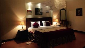 A bedroom with a bed, bedside lamps, a mirror, and wall art. - Puma Garden and Suites (Kigali)