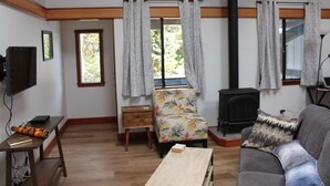Un salon avec un plancher en bois, un canapé, un fauteuil, une table, un téléviseur et une cheminée.