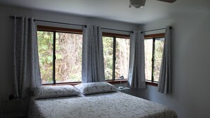 Une chambre à coucher avec un grand lit, deux fenêtres avec des rideaux, une table de chevet et une lampe.