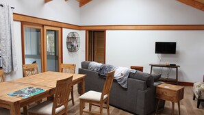 Un salon avec une table à manger en bois, des chaises, un canapé gris et un téléviseur posé sur un meuble en bois.