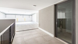 Un espacio interior amplio con puerta de vidrio, barandilla de metal y suelo de baldosas.