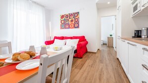 Una cocina moderna con armarios blancos, un sofá rojo y una mesa de comedor con platos y pasteles.