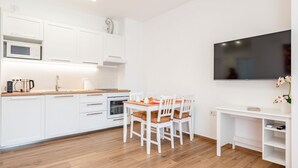 Una cocina moderna con armarios blancos, una mesa de comedor con sillas, un televisor de pantalla plana y un escritorio blanco con una planta.