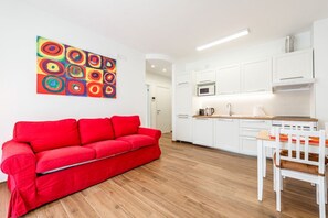A modern kitchen with white cabinets, a red sofa, and a colorful abstract painting.