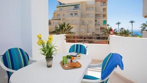 Een balkon met een tafel gedekt voor twee personen, stoelen, een bloempot en uitzicht op een gebouw en palmbomen.
