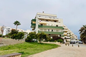 A multi-story residential building with balconies, a paved pathway, and parked cars.
