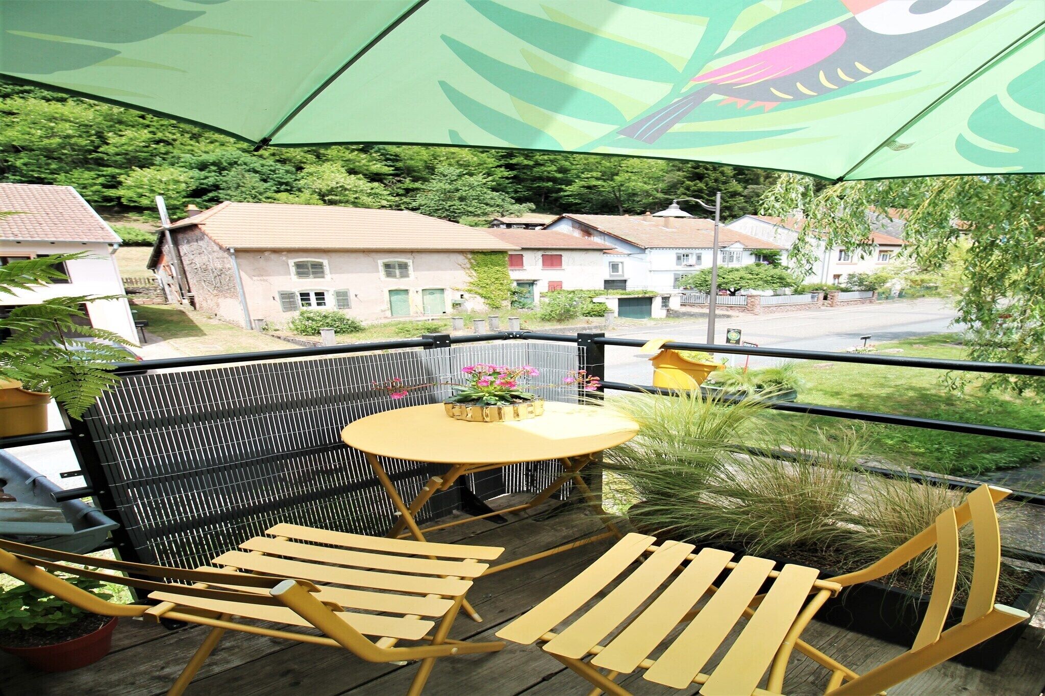 A balcony with a wooden chair, a small round table, and a green umbrella.