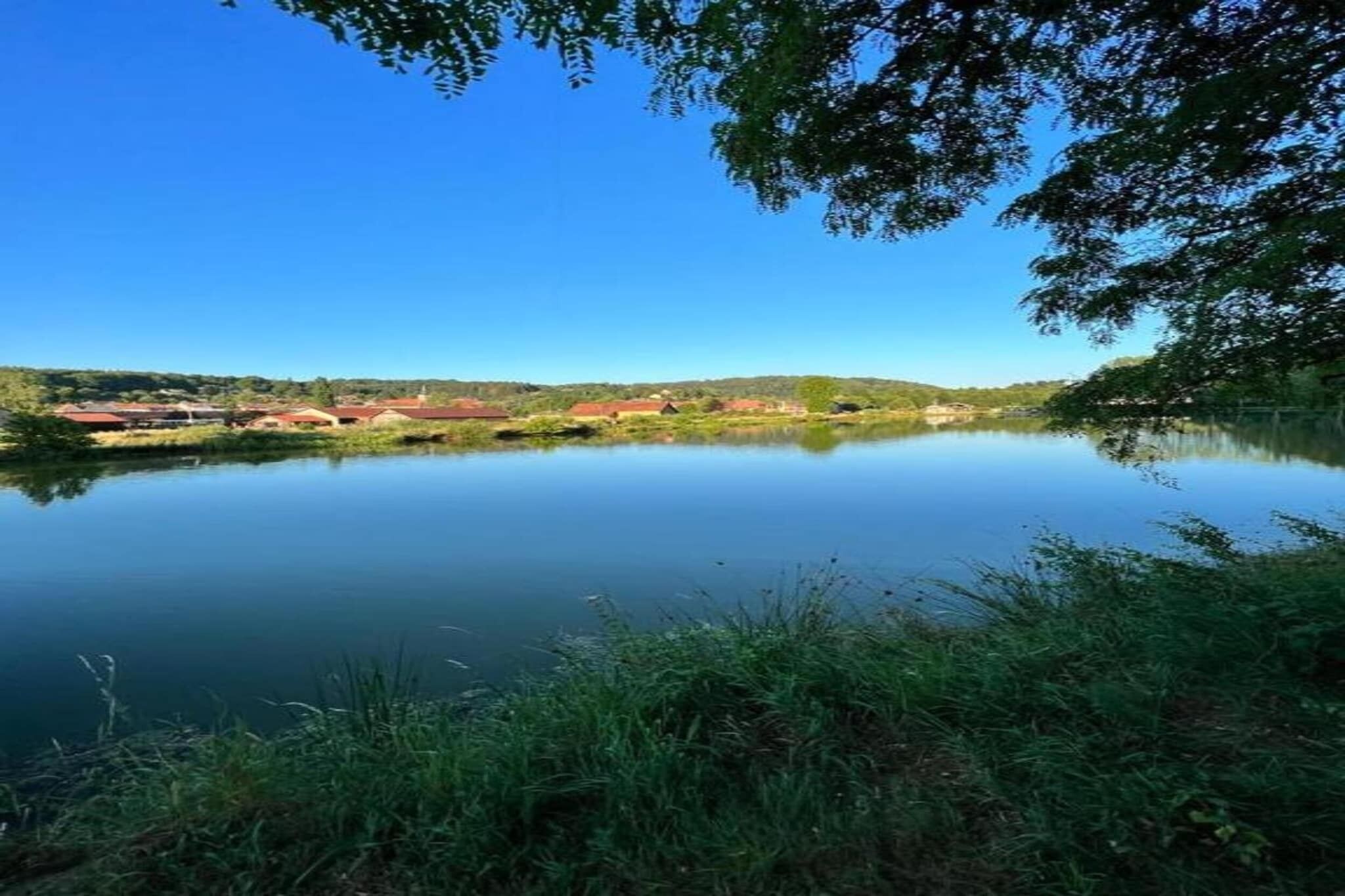 Un lago tranquilo con un reflejo nítido, rodeado de vegetación y edificios a la distancia.