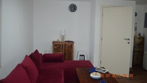 A living room with a red sofa, a wooden cabinet, a white door, and a wall clock.